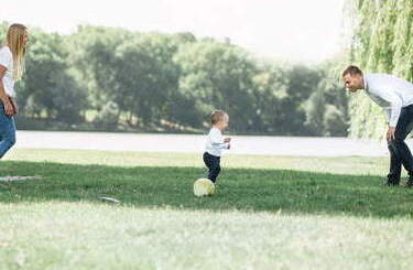 Rodzice grają z małym synkiem w piłkę na trawniku.
