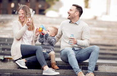 Rodzice siedzą z synkiem na schodach i puszczają bańki mydlane.